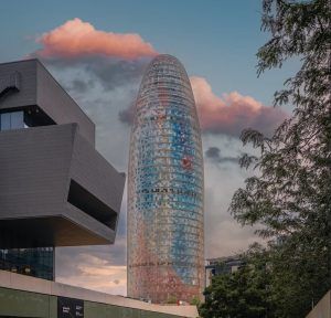 El rascacielos Mirador Torre Glorias, con su vibrante fachada, se alza contra un cielo nublado, rodeado de árboles y edificios. - ForTwo - Planes para parejas