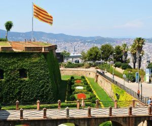 Encaramada en la cima de la colina, la fortaleza, con su bandera a rayas y sus exuberantes jardines, ofrece vistas panorámicas de Barcelona. Accesible a través del Teleférico de Barcelona, ofrece un mirador único que encapsula la esencia de la rica historia y la vibrante cultura de la ciudad. - ForTwo - Planes para parejas