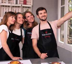 Cuatro personas con delantales se reúnen para una selfie grupal durante su Clase de cocina de paella en Barcelona. - ForTwo - Planes para parejas