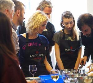 Personas vestidas con delantal se reunieron alrededor de una mesa con cuencos y vasos para la "Clase de cocina de paella en Barcelona", sumergiéndose en la elaboración de auténtica paella en medio de la vibrante escena culinaria de Barcelona. - ForTwo - Planes para parejas