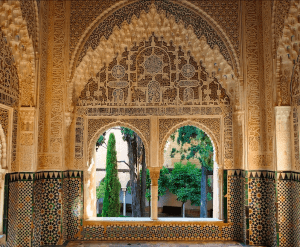 Una ventana arqueada intrincadamente tallada con detalles ornamentados da a un patio lleno de árboles, que recuerda la exquisita arquitectura que se ve con Entradas para Alhambra y Palacios Nazaríes: Visita guiada. - ForTwo - Planes para parejas