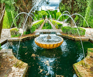 Bajo un cielo nublado, árboles y setos rodean la fuente circular de un jardín con arroyos de agua arqueados, haciendo eco de la belleza de las Entradas para Alhambra y Palacios Nazaríes: Visita guiada. - ForTwo - Planes para parejas
