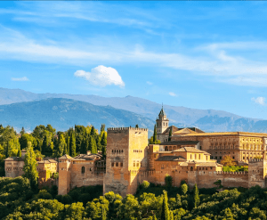 El palacio de la Alhambra en Granada, España, presenta majestuosamente los Palacios Nazaríes frente a vistas de montañas y un cielo azul claro. Opte por "Entradas para Alhambra y Palacios Nazaríes: Visita guiada" para experimentar plenamente su rica historia y su impresionante belleza. - ForTwo - Planes para parejas