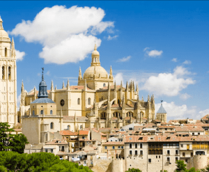 Experimente la grandeza de la Catedral de Segovia bajo un cielo azul, rodeada de edificios históricos y nubes esponjosas, con el majestuoso Alcázar de Segovia completando esta pintoresca escena en "Ávila y Segovia: Excursión de un día desde Madrid con Entrada al Alcázar de Segovia. - ForTwo - Planes para parejas