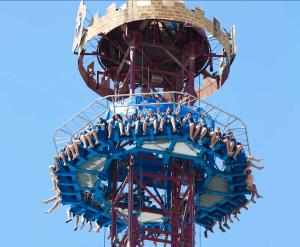 Los visitantes disfrutan del paseo en la torre de caída azul, con las piernas colgando contra un cielo despejado, en Isla Mágica Sevilla con un boleto de Entrada para Isla Mágica Sevilla. - ForTwo - Planes para parejas