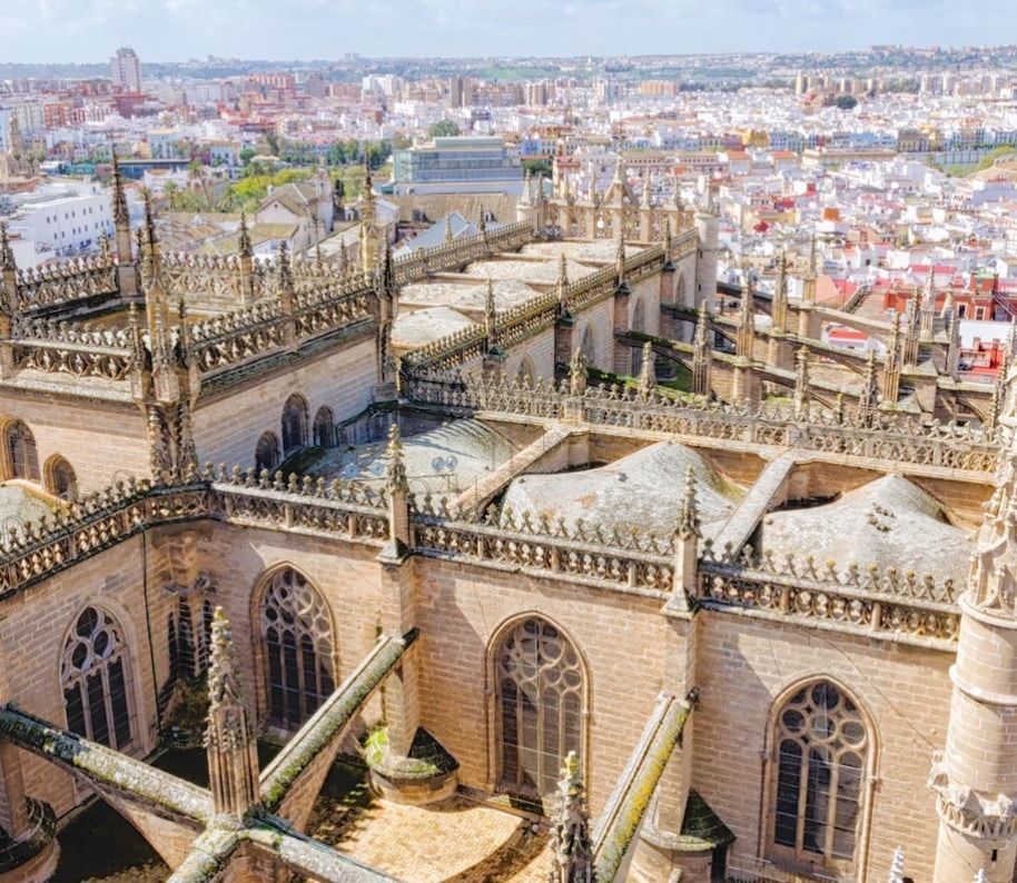 Una impresionante vista aérea de las intrincadas agujas góticas de la Catedral de Sevilla junto a la icónica Giralda, todo ello enmarcado por un vasto paisaje urbano. Disfrute de esta magnífica vista con nuestra entrada sin colas: Entrada a la Catedral de Sevilla y la Giralda (sin colas). - ForTwo - Planes para parejas