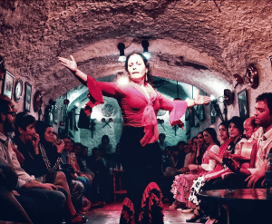 En el ambiente íntimo de las Cuevas del Sacromonte, un bailarín de flamenco actúa apasionadamente para el público, capturando la esencia del "Espectáculo Flamenco en las Cuevas del Sacromonte con Los Tarantos. - ForTwo - Planes para parejas