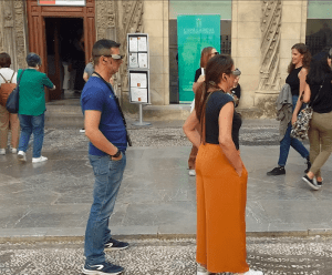 La gente se reúne frente a la ornamentada entrada de la Catedral de Granada para leer los paneles informativos y considerar comprar "Entradas a la Capilla y Catedral de Granada Visita guiada en Realidad Virtual" que da vida a la histórica Capilla. - ForTwo - Planes para parejas