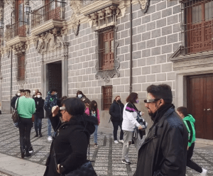 Un grupo se reúne frente a un edificio ornamentado con paredes de piedra y grandes puertas de madera, evocando la belleza que se ve en las "Entradas a la Capilla y Catedral de Granada Visita guiada en Realidad Virtual. - ForTwo - Planes para parejas