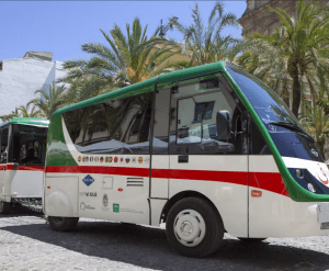Un pintoresco tren turístico, decorado con banderas verdes y blancas, se encuentra estacionado en una encantadora calle adoquinada adornada con elegantes palmeras en Granada. Entradas disponibles para el tren turístico en Granada. - ForTwo - Planes para parejas