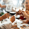 Personas levantando copas de vino en un brindis en una mesa de comedor con botellas y pan de Excursión y Cata de Vinos de la Ribera del Duero desde Madrid visibles, que recuerdan a una elegante cata de vinos. - ForTwo - Planes para parejas