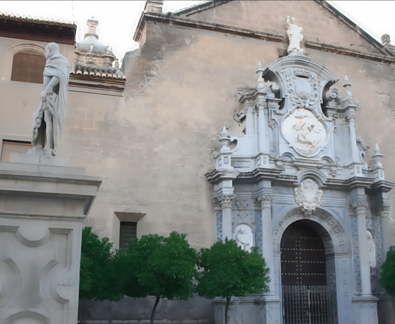 La ornamentada fachada de piedra del edificio, que evoca la Granada poética de García Lorca, presenta estatuas y tallas intrincadas, mientras que los árboles en primer plano invitan a un "Federico García Lorca: Tour guiado por Granada" a través de su belleza atemporal. - ForTwo - Planes para parejas