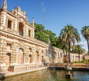 El Sevilla Super Combi presenta un diseño ornamentado con ventanas arqueadas, palmeras y una fuente, bellamente iluminada por el cálido resplandor del sol. - ForTwo - Planes para parejas