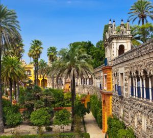 El Sevilla Super Combi adorna un edificio histórico de Sevilla, con arcos y exuberantes jardines donde las palmeras se mecen suavemente bajo un cielo azul claro. - ForTwo - Planes para parejas