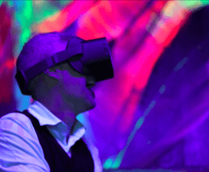 Una persona con un casco de realidad virtual se sumerge en un mundo vibrante, con luces de colores que iluminan la escena como la cautivadora experiencia de Entradas al Nomad Museo Inmersivo. - ForTwo - Planes para parejas