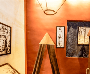 Una sala artística con bocetos enmarcados sobre paredes rojas y una estructura piramidal de madera evoca el encanto cautivador de Entradas sin colas al Palacio de los Olvidados. - ForTwo - Planes para parejas