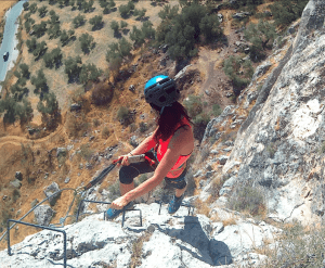 Vestido con equipo de escalada, la persona asciende por el acantilado rocoso en la visita guiada Entradas para Vía Ferrata de Moclín desde Granada, revelando impresionantes vistas panorámicas de caminos sinuosos y paisajes cubiertos de matorrales. - ForTwo - Planes para parejas