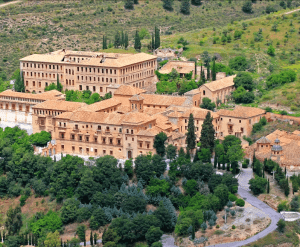 Una vista aérea muestra el entorno histórico de Visita la Abadía del Sacromonte + Museo Cuevas del Sacromonte, con sus edificios de piedra beige y sus vibrantes techos de color naranja enclavados en medio de una exuberante vegetación. - ForTwo - Planes para parejas