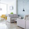 Una suite de GCE Hoteles ofrece una vida moderna con sofás beige, sillones amarillos, paredes gris claro, TV, iluminación colgante y luz natural, ideal para relajarse después de una escapada romántica en Cártama. - ForTwo - Planes para parejas