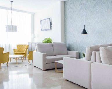 Una suite de GCE Hoteles ofrece una vida moderna con sofás beige, sillones amarillos, paredes gris claro, TV, iluminación colgante y luz natural, ideal para relajarse después de una escapada romántica en Cártama. - ForTwo - Planes para parejas
