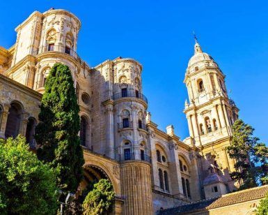 El Hilton Garden Inn en Málaga ofrece una escapada premium, ubicado entre catedrales históricas con una arquitectura ornamentada y árboles altos bajo un cielo azul claro, brindando una visión del rico pasado de Málaga. - ForTwo - Planes para parejas