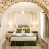Descubra la paz en Suites La Posada de Pilar, con un arco de piedra, una cama blanca y detalles en verde. Iluminada por lámparas en las mesitas de noche bajo una suave luz, es la escapada perfecta a Córdoba con patio cordobés. - ForTwo - Planes para parejas