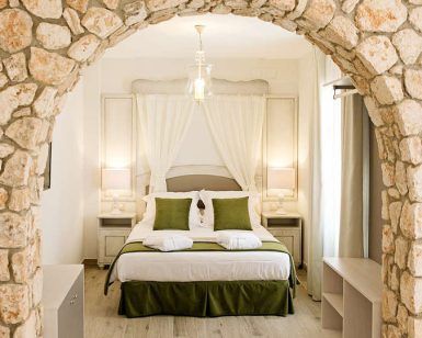 Descubra la paz en Suites La Posada de Pilar, con un arco de piedra, una cama blanca y detalles en verde. Iluminada por lámparas en las mesitas de noche bajo una suave luz, es la escapada perfecta a Córdoba con patio cordobés. - ForTwo - Planes para parejas