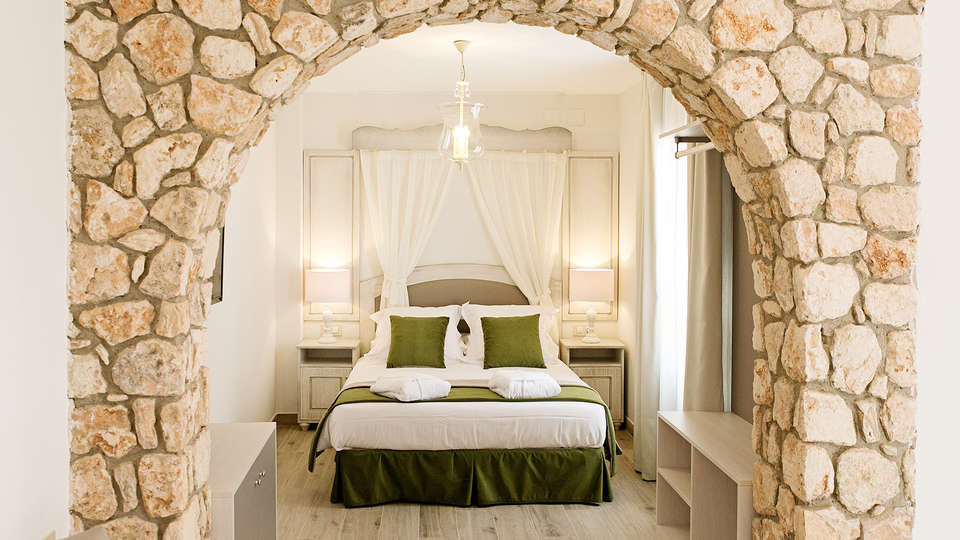 Descubra la paz en Suites La Posada de Pilar, con un arco de piedra, una cama blanca y detalles en verde. Iluminada por lámparas en las mesitas de noche bajo una suave luz, es la escapada perfecta a Córdoba con patio cordobés. - ForTwo - Planes para parejas