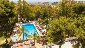 Vista aérea de una piscina rodeada de árboles y tumbonas, con vistas a la ciudad y al mar: un lugar perfecto para una pareja en una Escapada a Torremolinos en pareja con todo incluido. - ForTwo - Planes para parejas