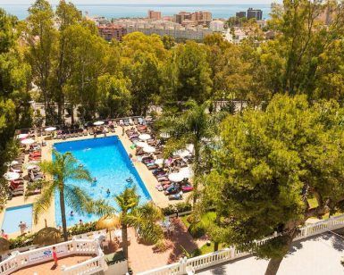 Vista aérea de una piscina rodeada de árboles y tumbonas, con vistas a la ciudad y al mar: un lugar perfecto para una pareja en una Escapada a Torremolinos en pareja con todo incluido. - ForTwo - Planes para parejas