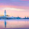 La serena puesta de sol en el puerto, con un faro y palmeras, enmarcada por barcos contra un cielo rosa y morado, es ideal para tu "Escapada a un apartahotel de Málaga: Soho Boutique Museo". Imagina disfrutar de esta vista después de explorar la vibrante ciudad. - ForTwo - Planes para parejas