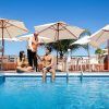 Un hombre y una mujer se relajan junto a la piscina del Hotel Globales Acuario, disfrutando de unas bebidas con un camarero cerca. Las sombrillas ofrecen sombra bajo el sol radiante: una escapada ideal a Tenerife. - ForTwo - Planes para parejas