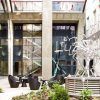 Un moderno patio en Budapest exhibe una escultura abstracta de metal, plantas en macetas y sillas redondas con un fondo de escalera de vidrio, ideal para una escapada romántica en el Hotel Continental 4 estrellas (Budapest). - ForTwo - Planes para parejas