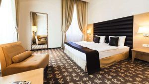 El Hotel Buda Castle Fashion, en el centro de Budapest, ofrece una habitación moderna con cama doble, sillón, espejo grande, alfombra texturizada e iluminación cálida. - ForTwo - Planes para parejas