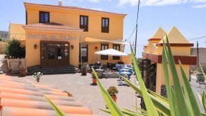Un pequeño hotel con una fachada amarilla, asientos al aire libre y un letrero que dice Hotel El Tejar bajo el cielo azul de Tenerife, ideal para una "Escapada en pareja a Tenerife: spa, vistas al mar y cava". - ForTwo - Planes para parejas