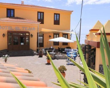 Un pequeño hotel con una fachada amarilla, asientos al aire libre y un letrero que dice Hotel El Tejar bajo el cielo azul de Tenerife, ideal para una "Escapada en pareja a Tenerife: spa, vistas al mar y cava". - ForTwo - Planes para parejas