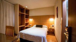 Cómoda habitación en Escapada en el centro de Córdoba: hotel Serrano con cama doble, estanterías de madera, iluminación cálida y una pequeña mesa con silla, ideal para tu escapada al centro de la ciudad. - ForTwo - Planes para parejas