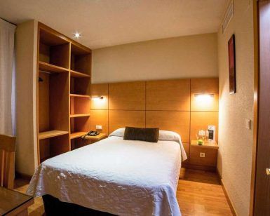 Cómoda habitación en Escapada en el centro de Córdoba: hotel Serrano con cama doble, estanterías de madera, iluminación cálida y una pequeña mesa con silla, ideal para tu escapada al centro de la ciudad. - ForTwo - Planes para parejas