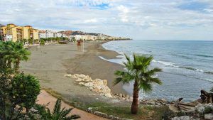 Experimente las vistas frente al mar de una costa de arena, palmeras y edificios cercanos bajo un cielo nublado, a solo unos pasos del Hotel Rincón Sol en el hermoso Rincón de la Victoria en la Costa del Sol. - ForTwo - Planes para parejas