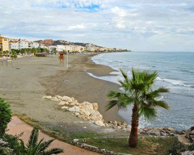 Experimente las vistas frente al mar de una costa de arena, palmeras y edificios cercanos bajo un cielo nublado, a solo unos pasos del Hotel Rincón Sol en el hermoso Rincón de la Victoria en la Costa del Sol. - ForTwo - Planes para parejas