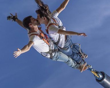 Dos personas hacen puenting en tándem, abrazándose en el aire contra el cielo azul claro y disfrutando de la emoción del "Puenting o Salto Bungee Jumping en pareja en Barcelona". - ForTwo - Planes para parejas