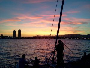 Disfruta de un perfecto "Paseo romántico en Catamarán Barcelona" con siluetas al atardecer contra un cielo vibrante y el impresionante skyline de Barcelona. - ForTwo - Planes para parejas