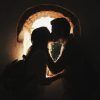 La silueta de una pareja se besa junto a una ventana en arco iluminada por el sol, encarnando la esencia de "Reportajes románticos de parejas en Granada". - ForTwo - Planes para parejas