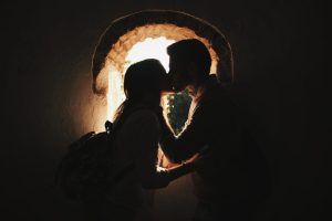 La silueta de una pareja se besa junto a una ventana en arco iluminada por el sol, encarnando la esencia de "Reportajes románticos de parejas en Granada". - ForTwo - Planes para parejas