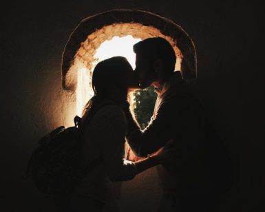 La silueta de una pareja se besa junto a una ventana en arco iluminada por el sol, encarnando la esencia de "Reportajes románticos de parejas en Granada". - ForTwo - Planes para parejas