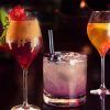 Experimente la rica coctelería de Barcelona con Taller de Coctelería: Aprende a Preparar y Degustar 3 Cócteles Exclusivos, que presenta un elegante cóctel con guarnición de fresas, uno con arándanos frescos y una pajita, y una obra maestra en tonos naranjas. - ForTwo - Planes para parejas