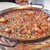 Una sartén con la tradicional paella de marisco, gambas y verduras, que recuerda a los sabores del Restaurante 7 Portes (Barcelona), reposa elegantemente sobre una cesta tejida. - ForTwo - Planes para parejas