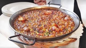 Una sartén con la tradicional paella de marisco, gambas y verduras, que recuerda a los sabores del Restaurante 7 Portes (Barcelona), reposa elegantemente sobre una cesta tejida. - ForTwo - Planes para parejas