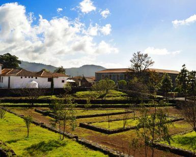 Disfrute de un paisaje pintoresco en La Casona del Patio, con exuberantes campos, linderos de piedra, árboles y encantadores edificios bajo un cielo azul nublado. Este idílico entorno encarna una auténtica "Escapada rural en Santiago del Teide". - ForTwo - Planes para parejas