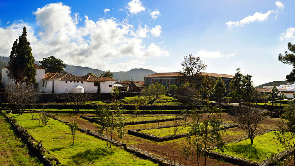 Disfrute de un paisaje pintoresco en La Casona del Patio, con exuberantes campos, linderos de piedra, árboles y encantadores edificios bajo un cielo azul nublado. Este idílico entorno encarna una auténtica "Escapada rural en Santiago del Teide". - ForTwo - Planes para parejas